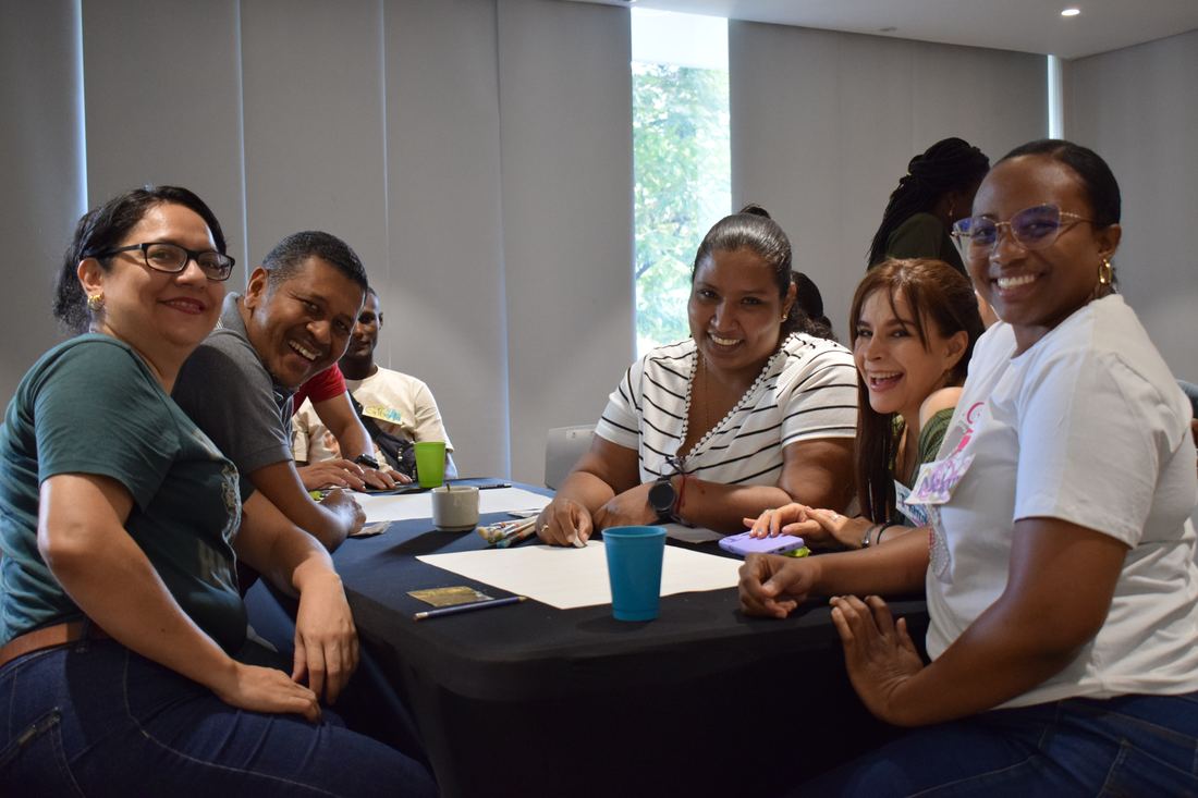 Un equipo de trabajo sonríe alrededor de una mesa durante un taller de habilidades blandas de Simoné