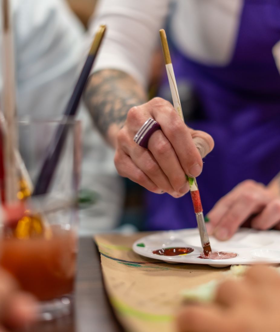 Mano de una participante mezclando pintura en una paleta durante un evento
